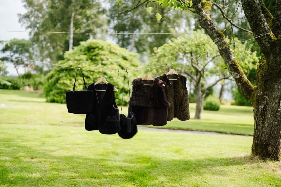 Handmade sheepskin vests and bags hung on a line between garden trees