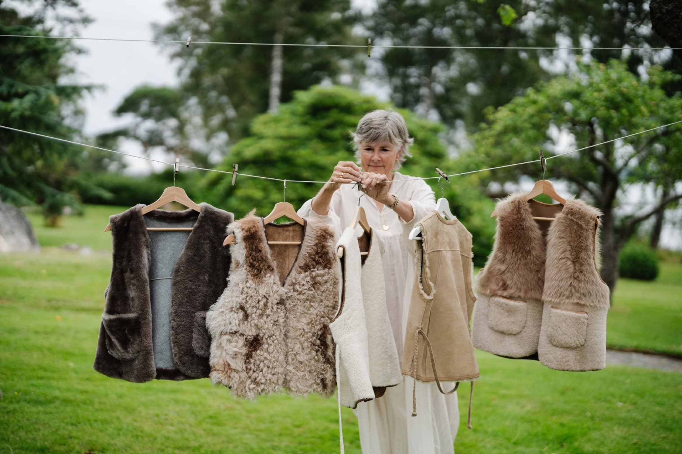 Birgitta Svensson hanging a row of handmade sheepskin and shearling vests on a garden line in Western Sweden