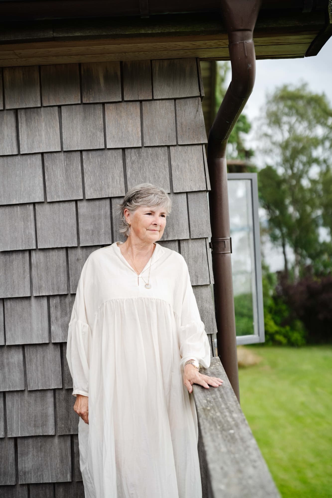 Birgitta Svensson standing beside a weathered timber cabin in the Swedish countryside