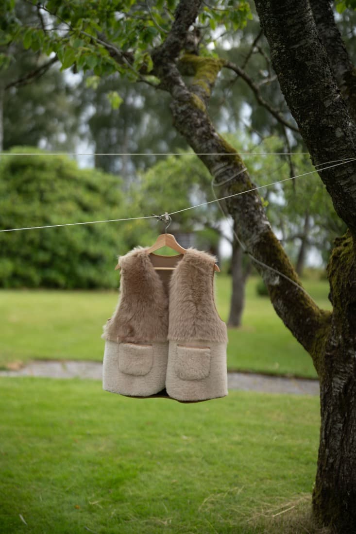 Handmade two-tone shearling vest with a cream wool body, taupe sheep-fur yoke and patch pockets, hanging outdoors