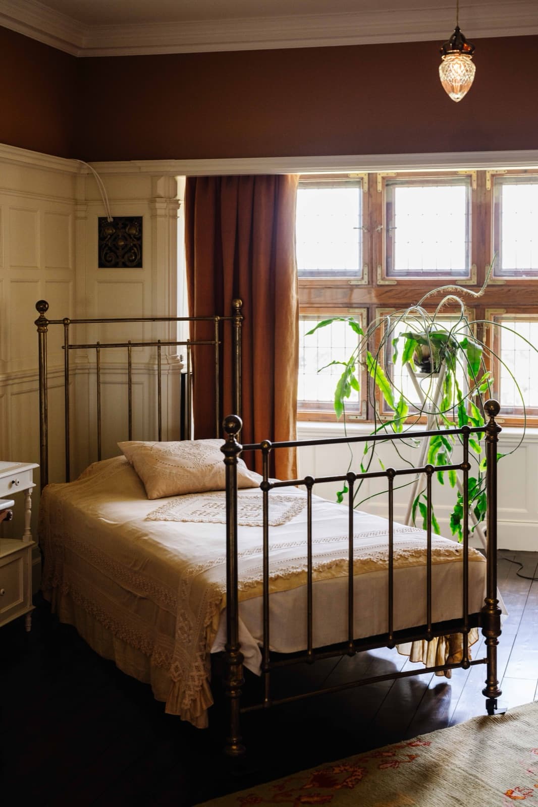A brass bed in a light-filled bedroom at Tjolöholm, houseplants at the window