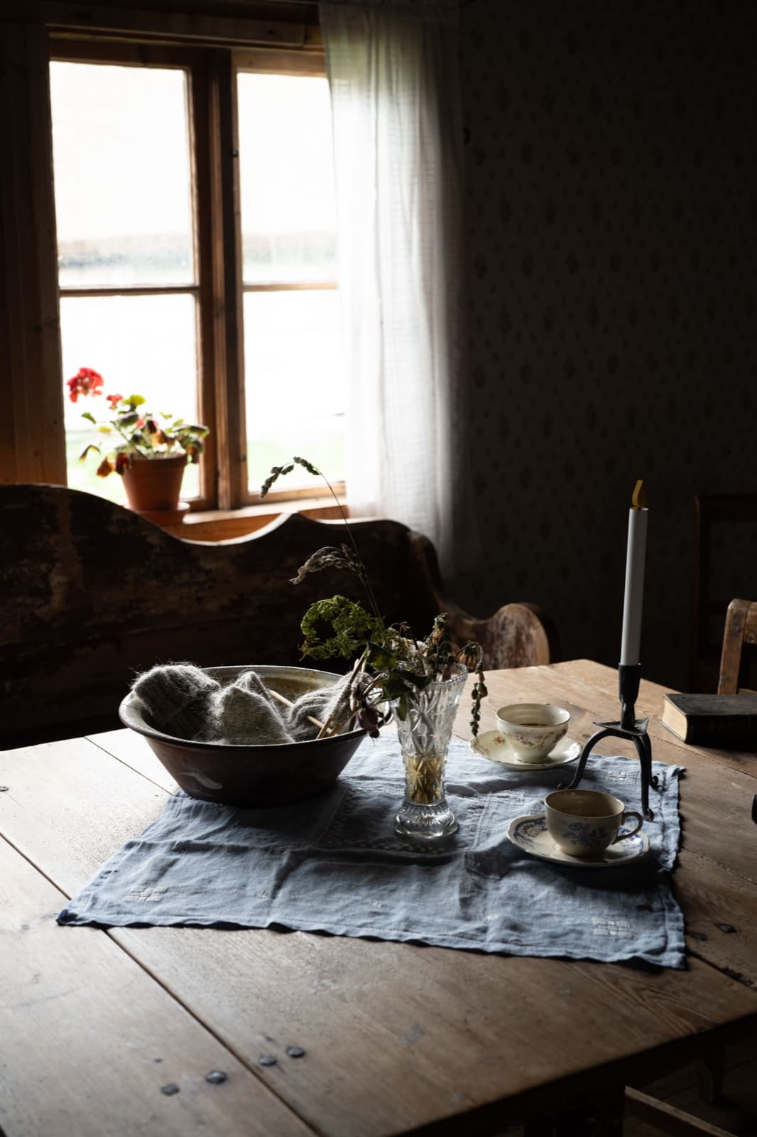 A wooden table with a linen runner, bowl and candlestick inside a workers' village cottage at Tjolöholm
